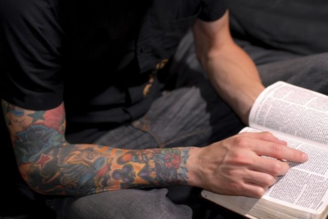 man in black t-shirt reading a book. his right arm is a tattoo sleeve